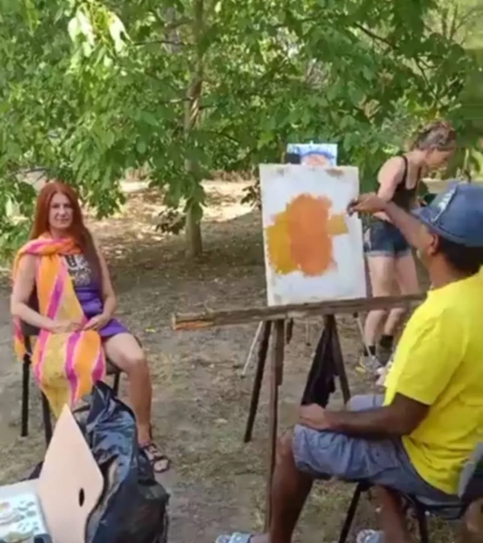 Outdoor live painting session with a seated model and an easel under trees